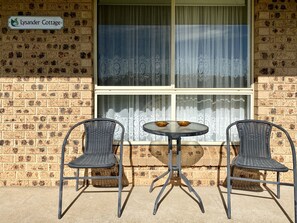 Two wicker chairs and a small round table outside a building with a brick facade and a sign reading "Lysander Cottage." - Titania Motel (Oberon)