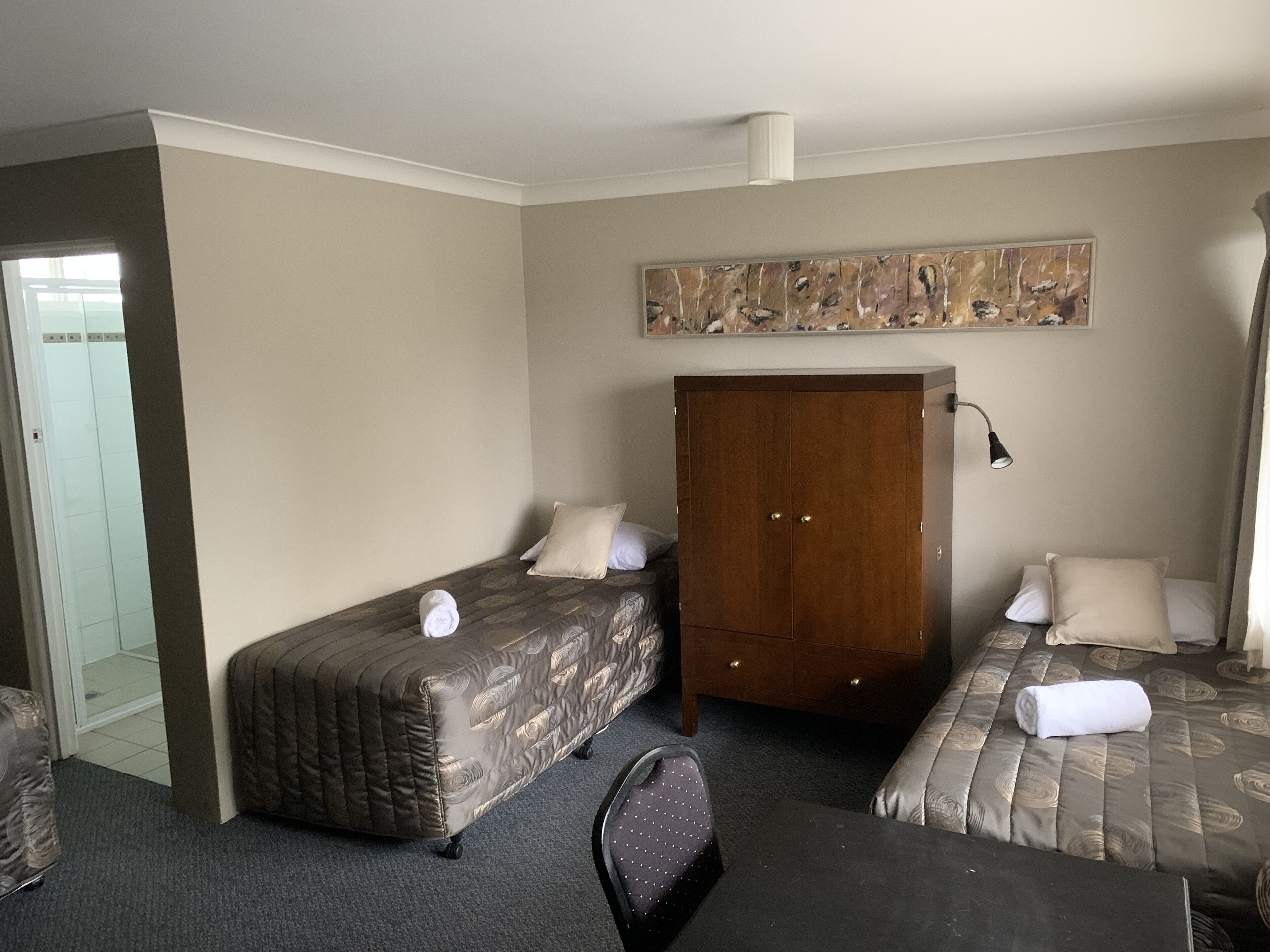 A hotel room with two beds, a wardrobe, a desk, and a chair.