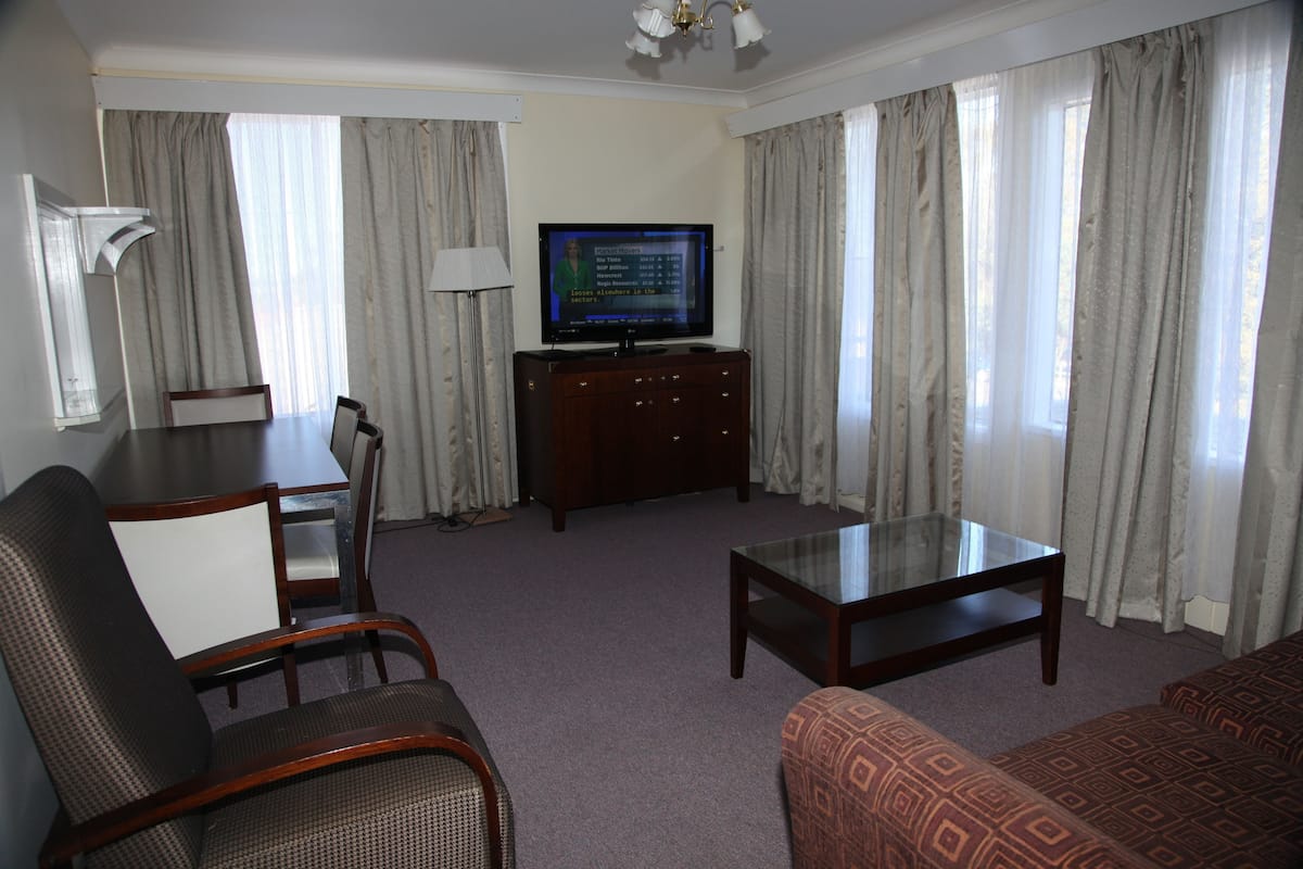 Una habitación de hotel con una mesa de comedor, dos sillas, un sofá, un televisor y un armario.