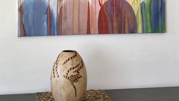 A colorful abstract painting on a wall with a textured vase on a woven placemat below.