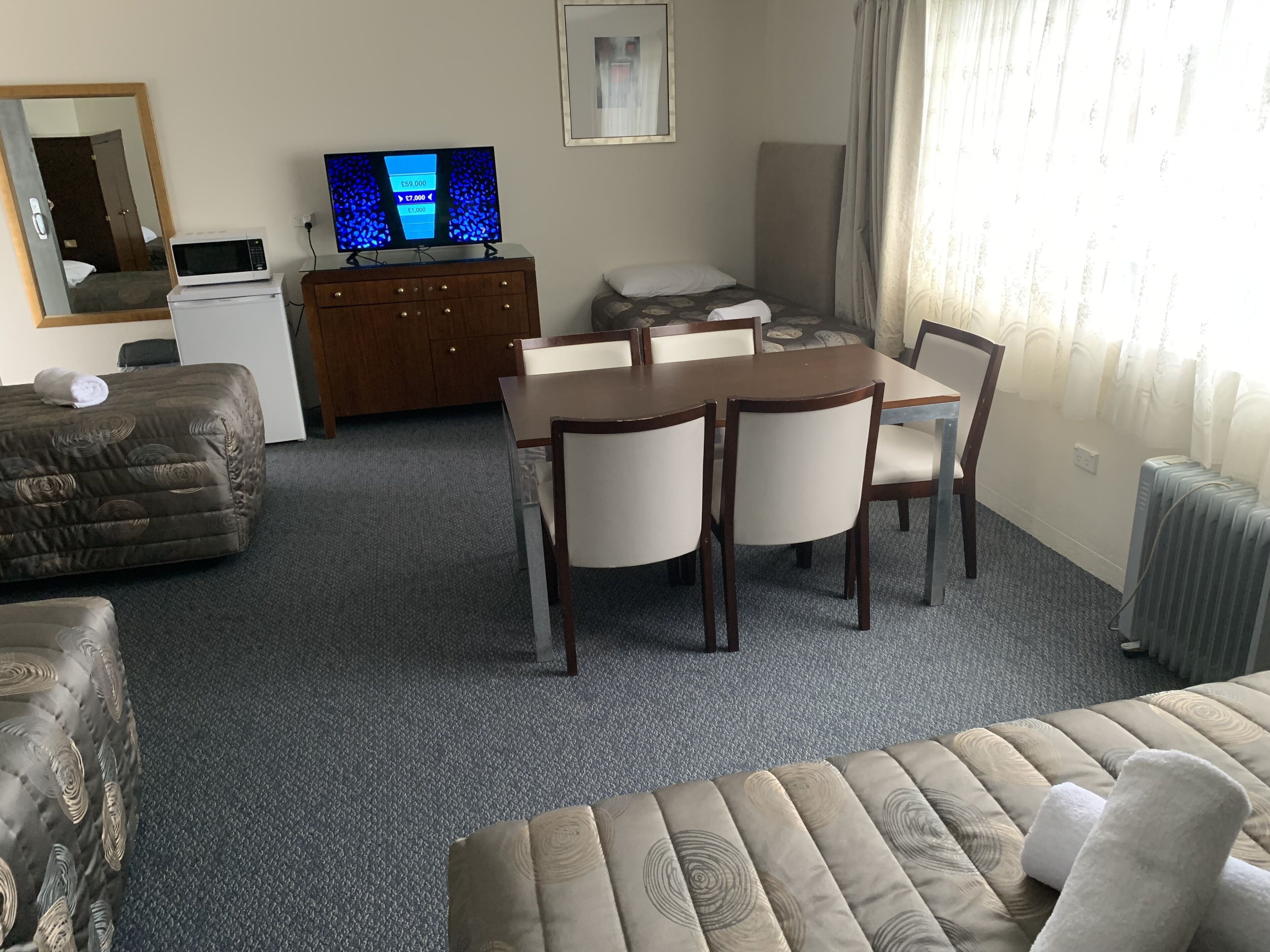 A hotel room with a dining table, chairs, a sofa, a TV, and a small kitchenette.