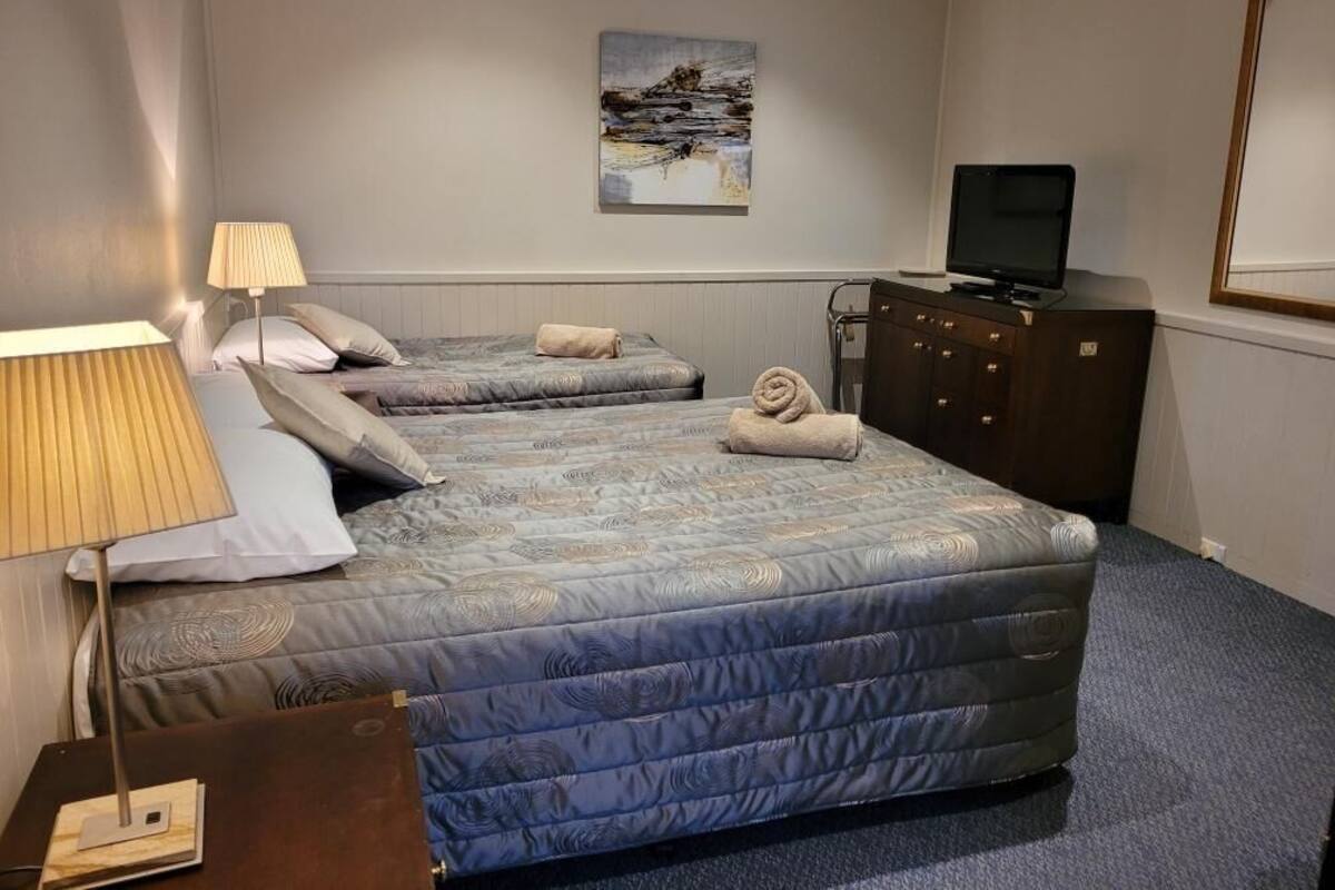 Habitación de hotel con dos camas, un televisor, un aparador y un cuadro en la pared.