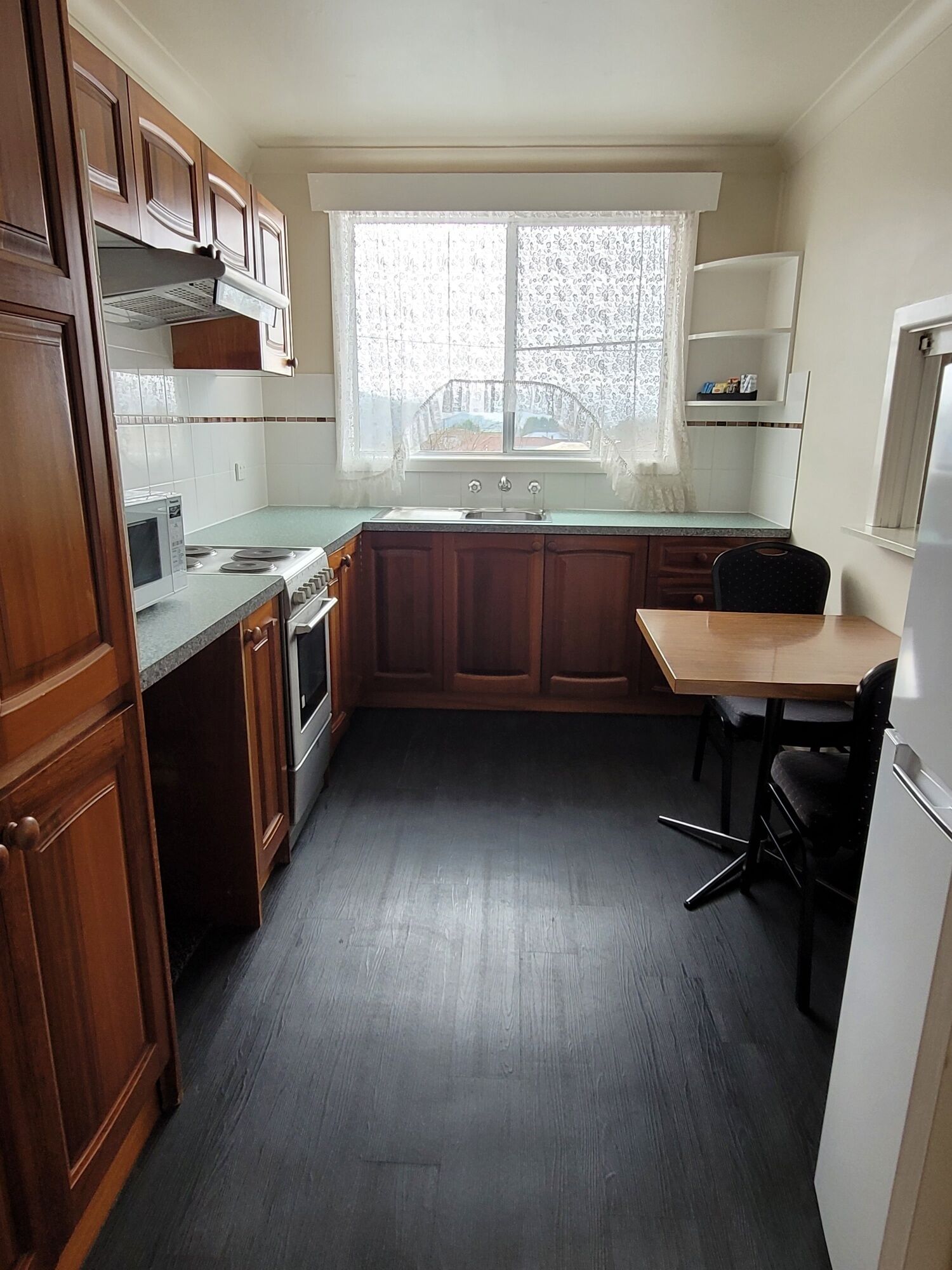 A compact kitchen with wooden cabinets, a built-in microwave, a sink, and a dining area with a chair.