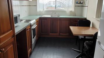 A compact kitchen with wooden cabinets, a built-in microwave, a sink, and a dining area with a chair.