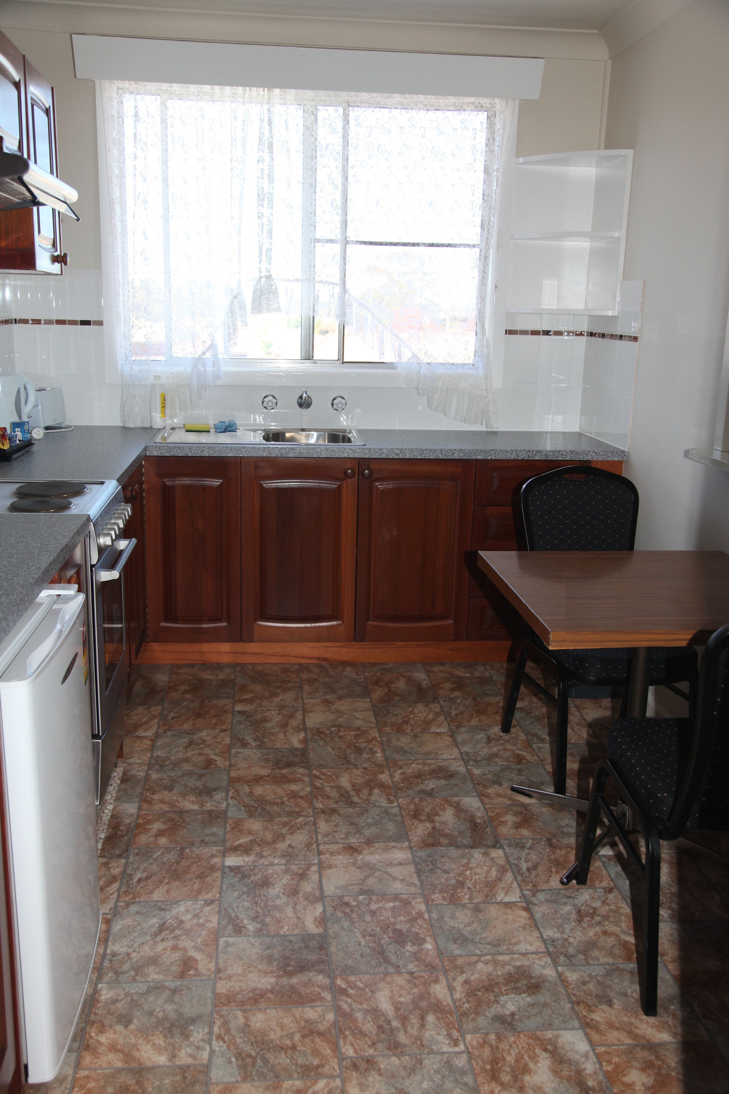 Una cocina con armarios de madera, un lavamanos, una estufa y un comedor con sillas.