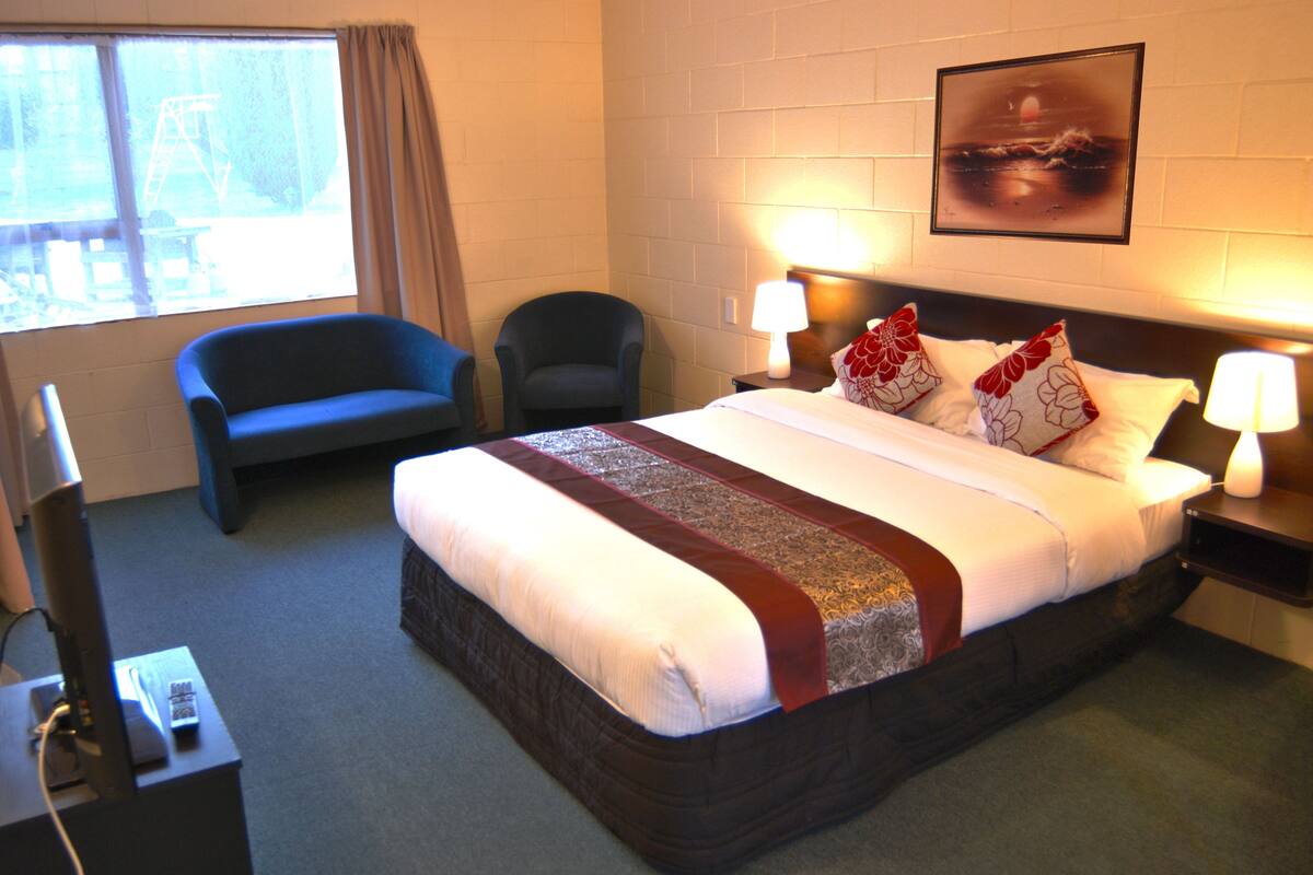 A hotel room with a large bed, two bedside lamps, a chair, and a TV.