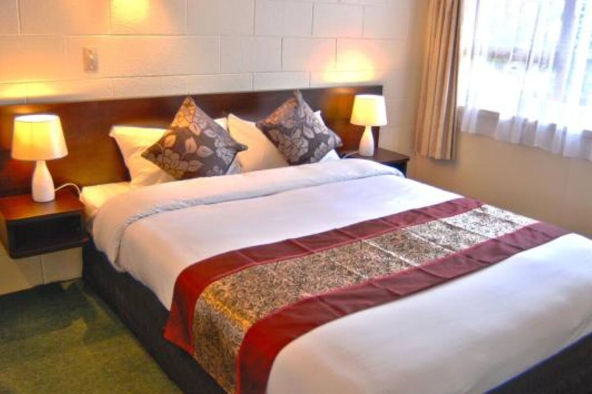 A neatly made bed with a patterned bedspread and pillows, two bedside lamps, and a window with curtains.