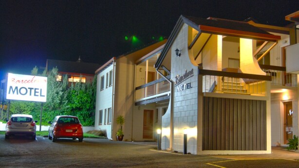 Un motel amb un rètol gran, un vestíbul cobert i dos cotxes aparcats al davant.