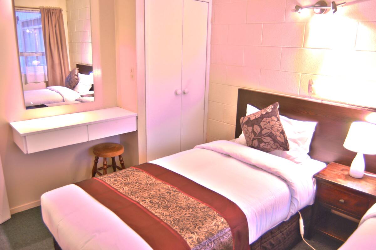 A hotel room with a bed, a nightstand, a mirror, a wardrobe, and a window with curtains.