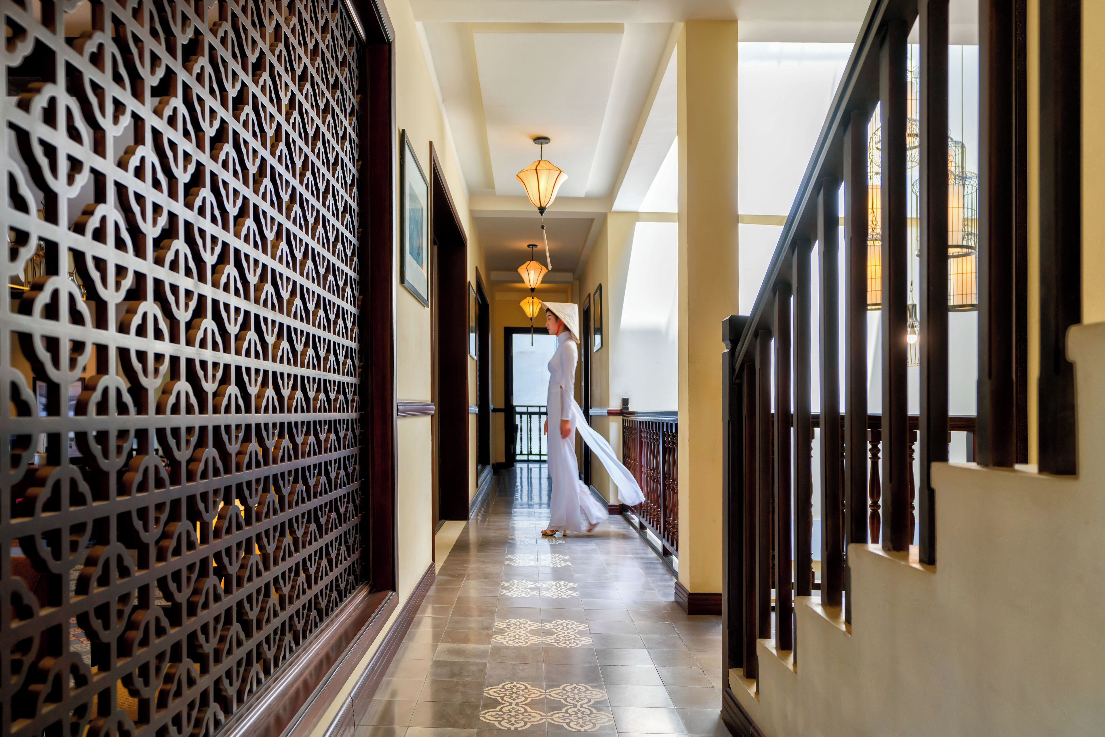 A corridor with patterned wall panels, a staircase, and a person walking.
