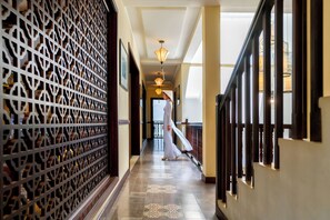 A corridor with patterned wall panels, a staircase, and a person walking. - Little Hoi An. A Boutique Hotel & Spa (Da Nang)
