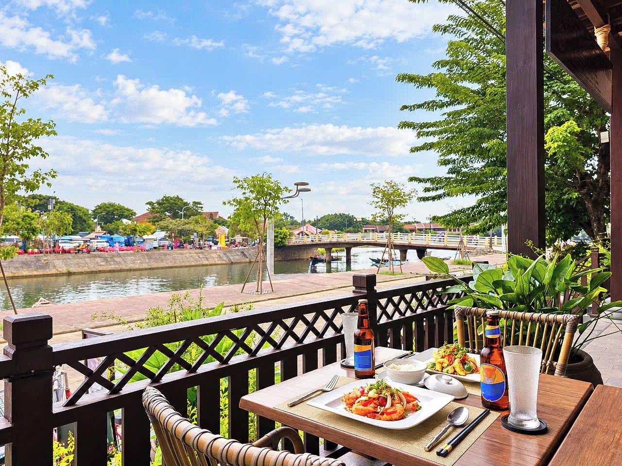Une table à manger dressée avec un repas, une bouteille et un verre, sur une terrasse donnant sur une rivière.