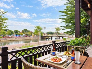 Une table à manger dressée avec un repas, une bouteille et un verre, sur une terrasse donnant sur une rivière.