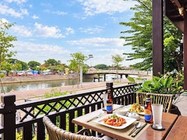 A dining table with a meal, a bottle, and a glass on a terrace overlooking a river.