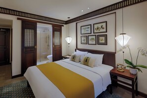 Une chambre d’hôtel avec un grand lit, une table de chevet avec une lampe, une orchidée en pot et des tableaux encadrés au mur.