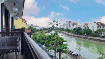 A balcony with wicker furniture, overlooking a river with buildings and trees in the background.