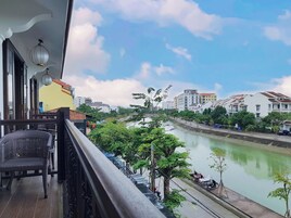 Un balcón con mobiliario de mimbre, con vista a un río con edificios y árboles al fondo.