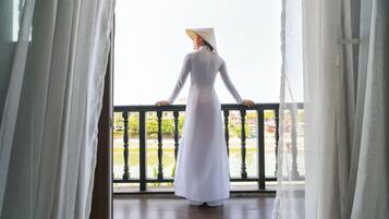 Eine Person in einem weißen Kleid steht auf einem Balkon mit Blick auf einen Park und Gebäude.