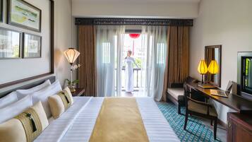 A hotel room with a bed, desk, chair, TV, and a view of the outside.