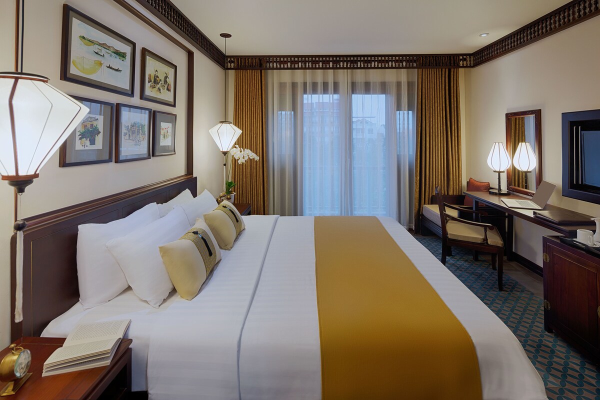 Une chambre d’hôtel avec un grand lit, un bureau, une chaise, une télévision et des tableaux encadrés accrochés au mur.