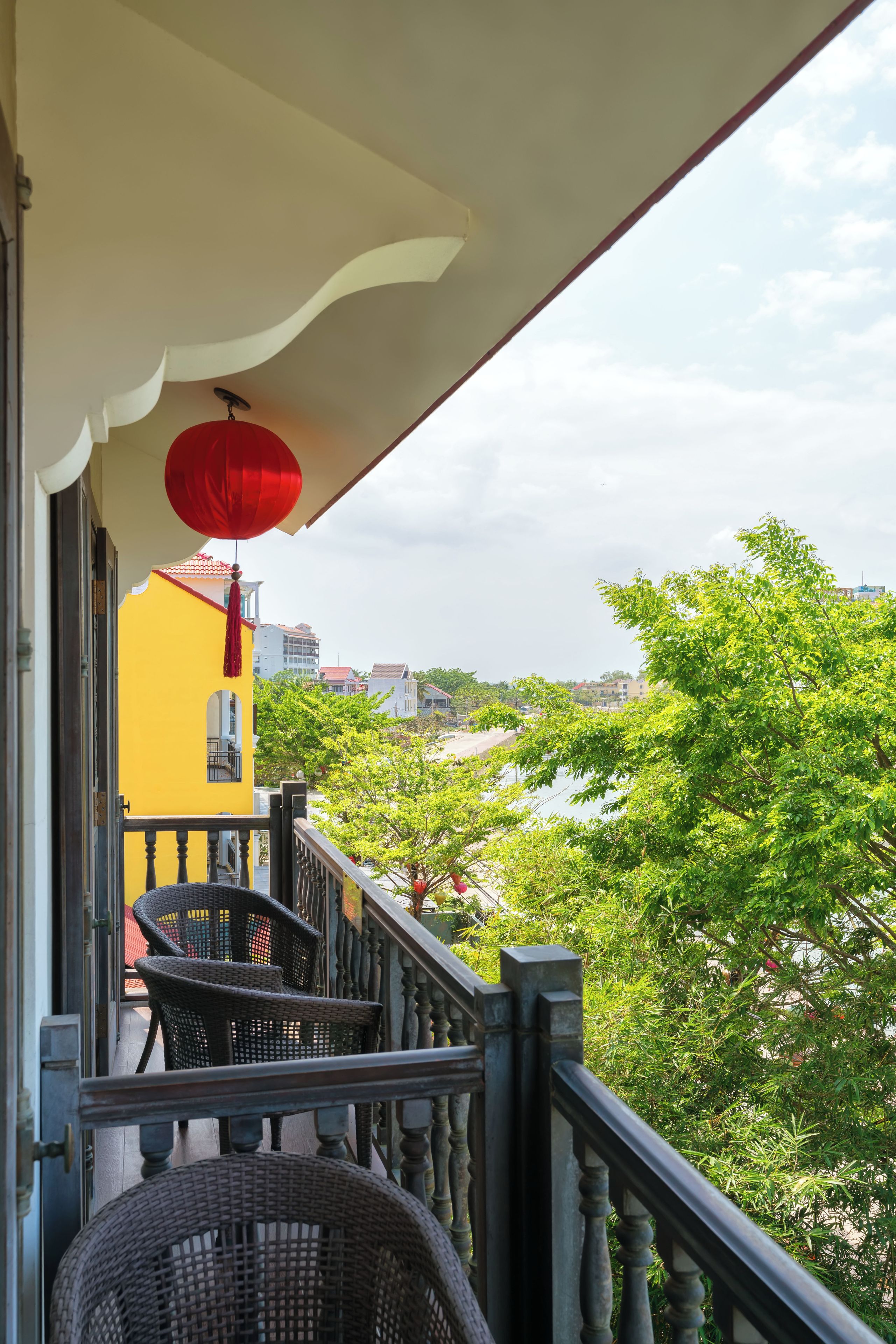 Un balcon agrémenté de meubles en osier, d’une lanterne rouge et offrant une vue sur une rivière et des bâtiments.