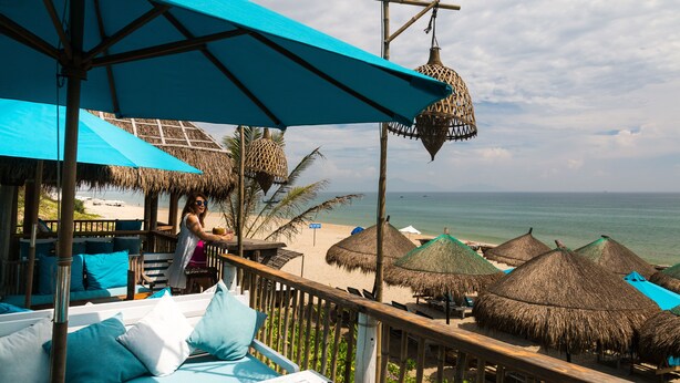 Een strandlounge met rieten parasols, een houten terras en uitzicht op de oceaan.