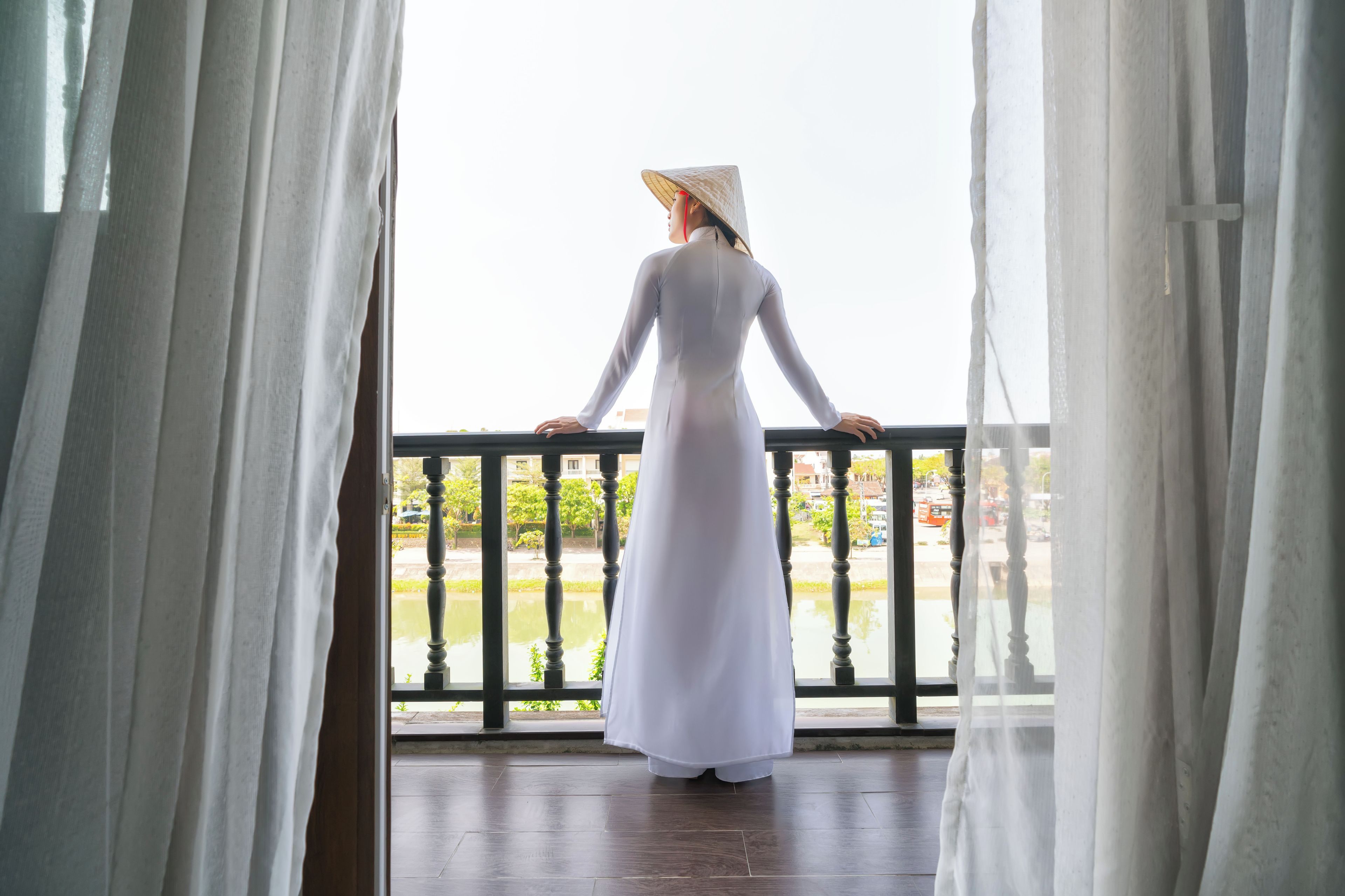 A person standing on a balcony with a view of a body of water and greenery.