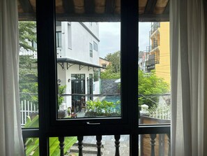 Vue depuis un balcon avec une porte vitrée, donnant sur une cour avec une piscine, un bâtiment blanc et, au fond, un bâtiment jaune.