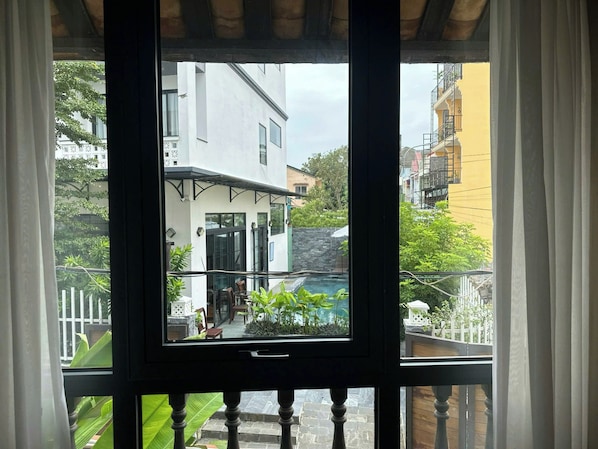 Udsigt fra en balkon med en glasdør, over en gårdhave med en pool, en hvid bygning og en gul bygning i baggrunden.
