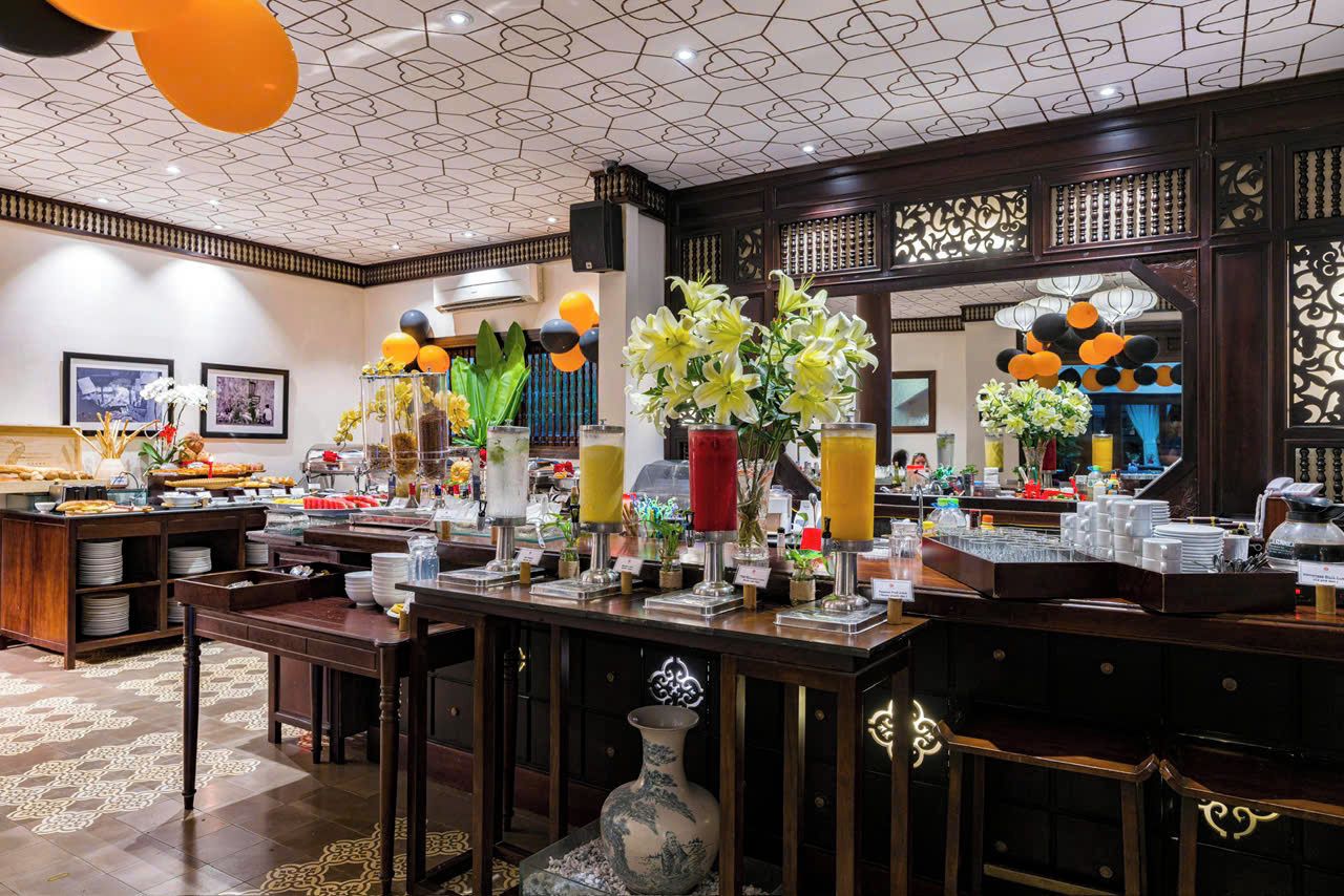A hotel breakfast area with a buffet setup, a coffee station, and decorative elements like flowers and lanterns.