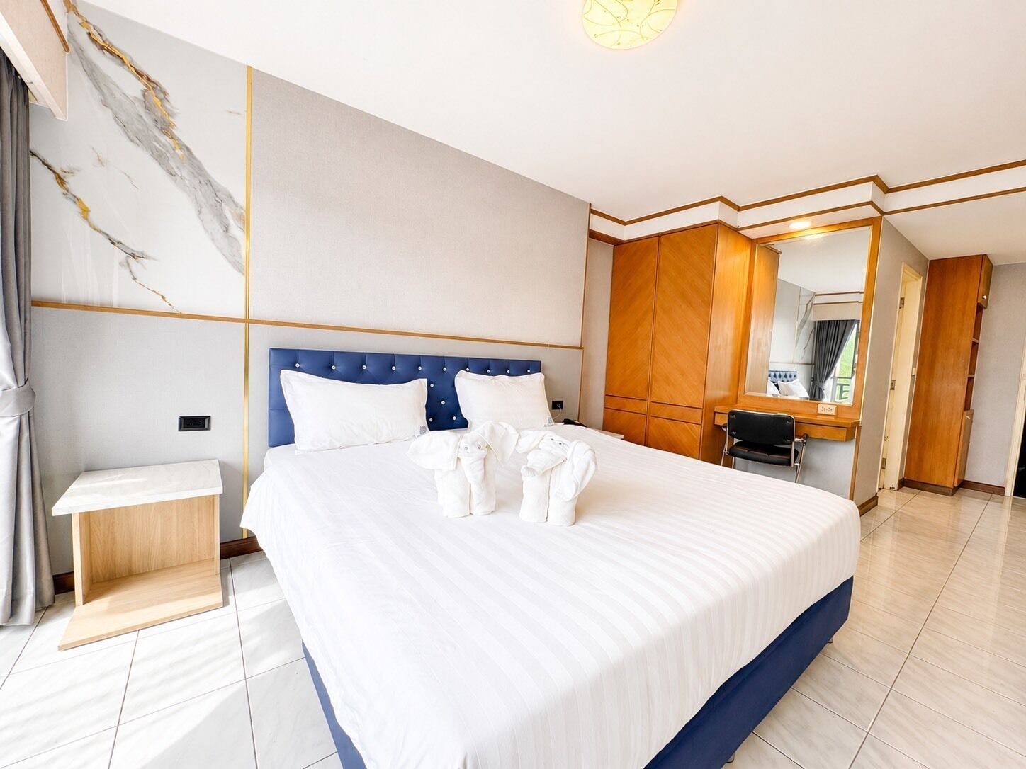 Quarto de hotel com uma cama grande, um guarda-roupa de madeira, uma mesinha de cabeceira e um espelho.