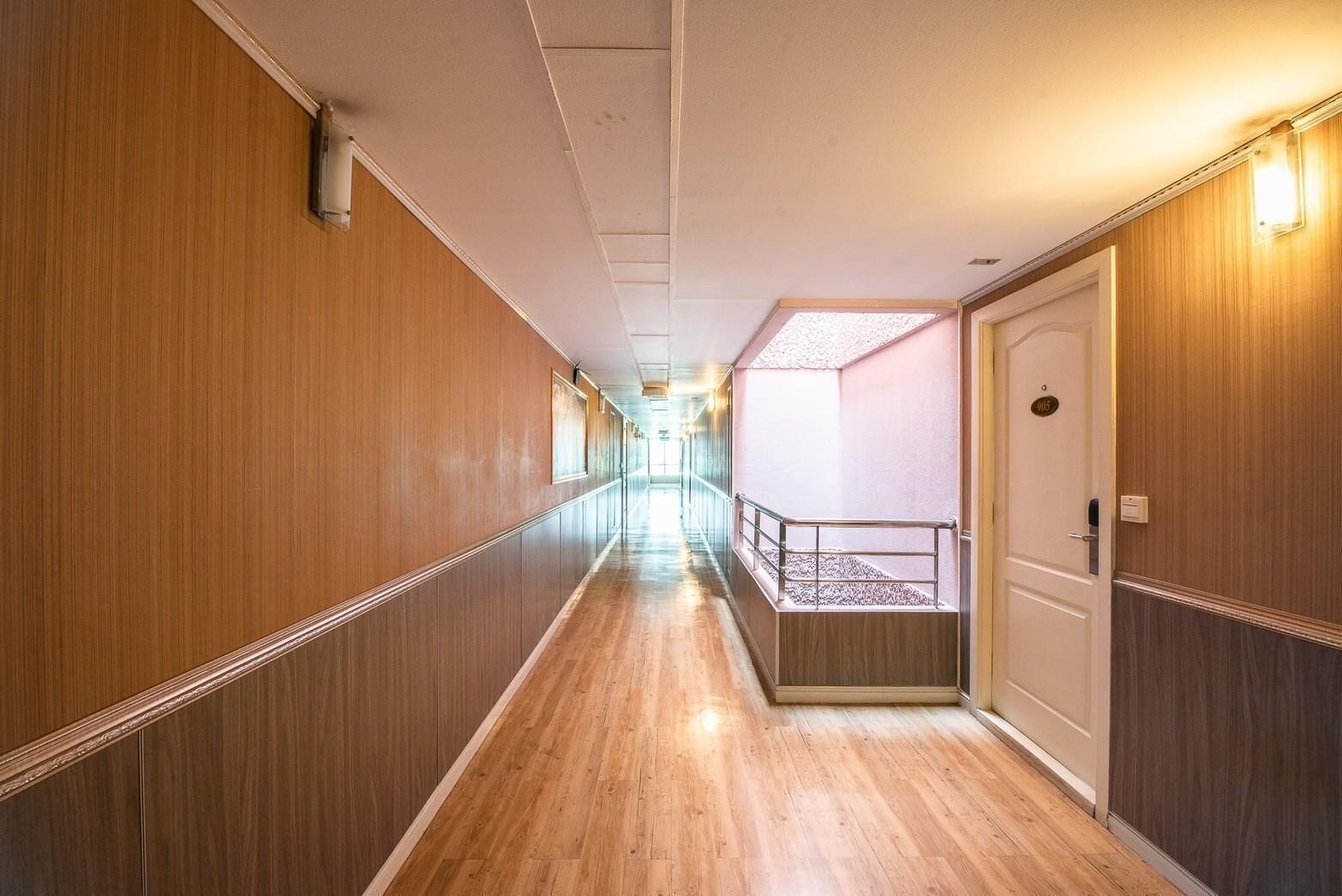 Un pasillo de hotel con paneles de madera, barandilla de vidrio y una puerta con un letrero.