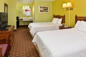 A hotel room with two beds, a television, a sink, and a painting on the wall.