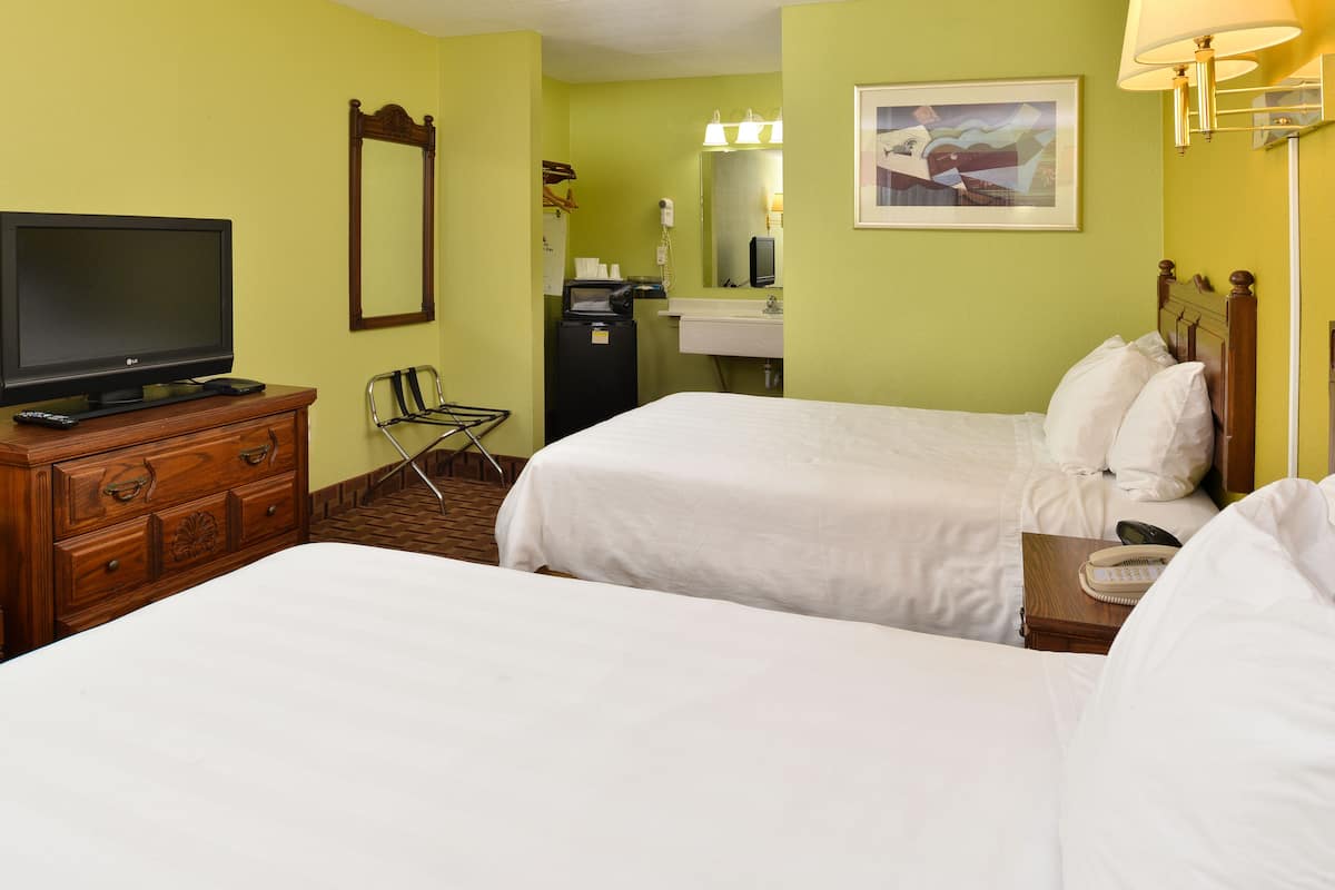 A hotel room with two beds, a TV, a desk with a lamp, a mirror, and a painting on the wall.