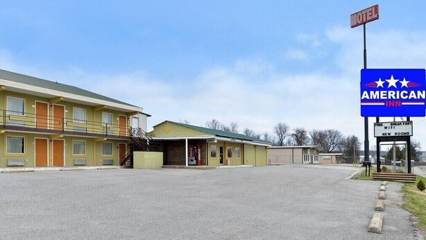 A motel with a sign for American Inn, featuring a parking lot and a building with multiple rooms.