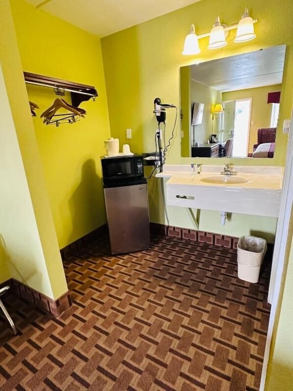 Une salle de bain avec un mur jaune, un lavabo avec un miroir, un sèche-cheveux et une poubelle.