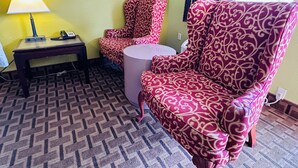 Ein Hotelzimmer mit einem gemusterten Sessel, einem kleinen runden Tisch, einer Lampe und einem Telefon.