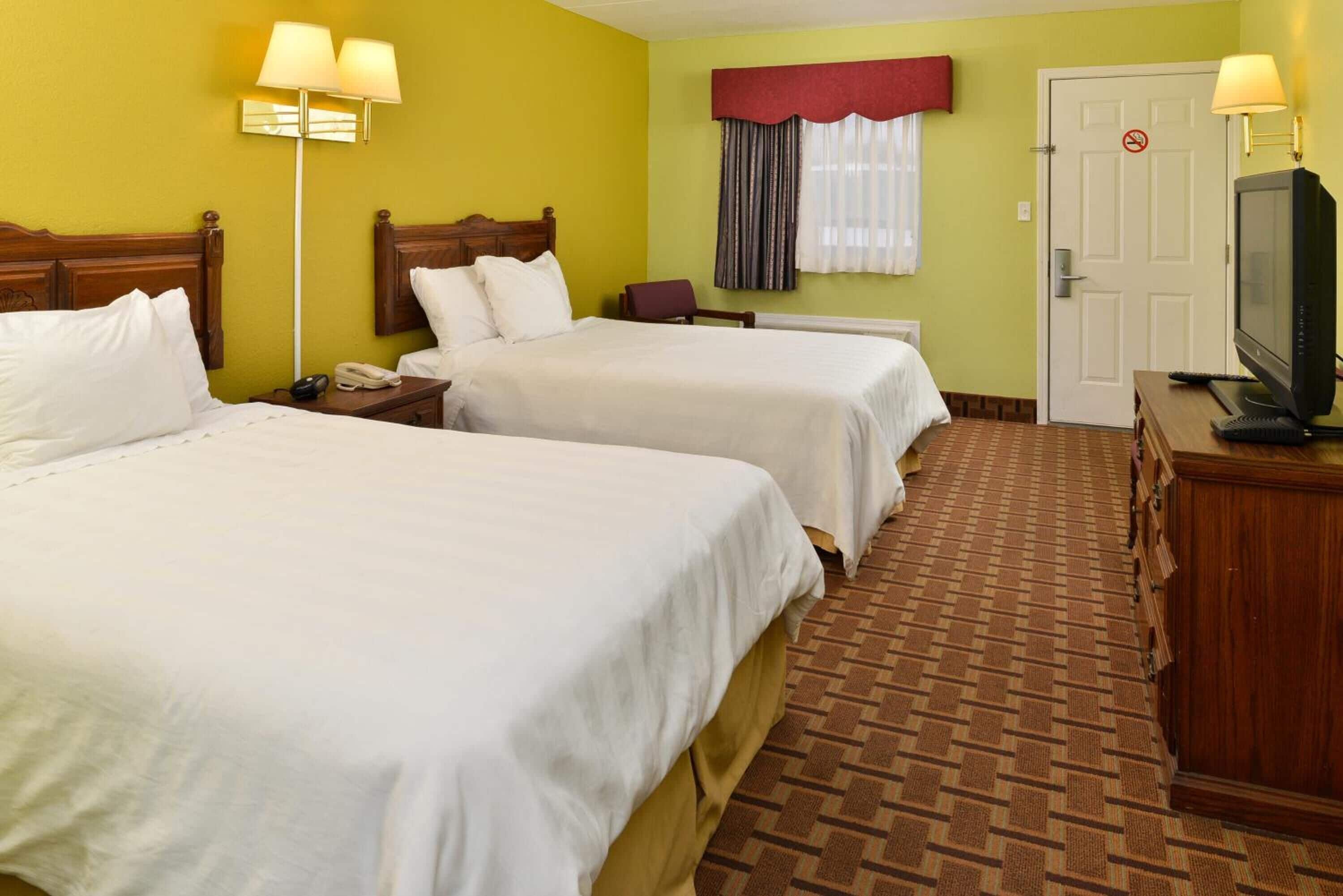 A hotel room with two beds, a television, a desk, and a lamp.