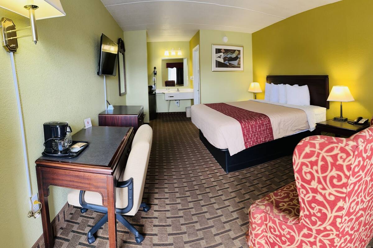 A hotel room with a bed, desk, chair, and a bathroom in the background.