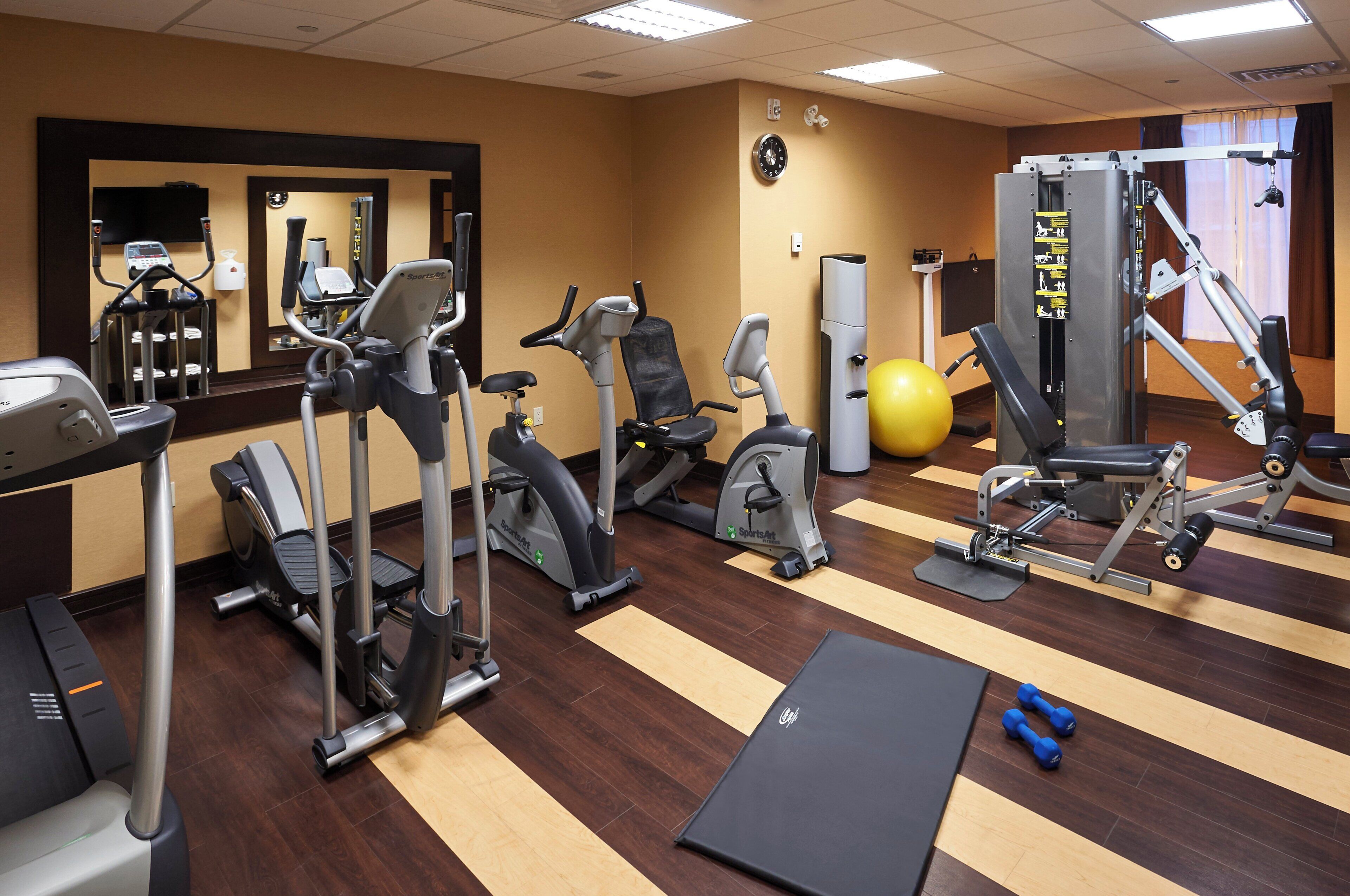 Un gimnasio con varios equipos de ejercicio, incluyendo cintas de correr, elípticas y pesas libres.
