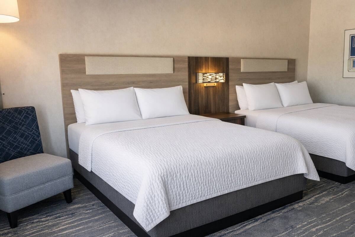 A hotel room with two beds, a small seating area, and a wall-mounted light fixture.