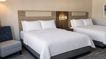 Habitación de hotel con dos camas, una zona de estar pequeña y una lámpara fijada a la pared.
