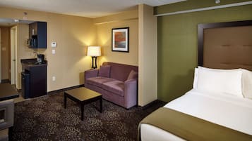 A hotel room with a bed, a sofa, a coffee machine, a desk, and a lamp.