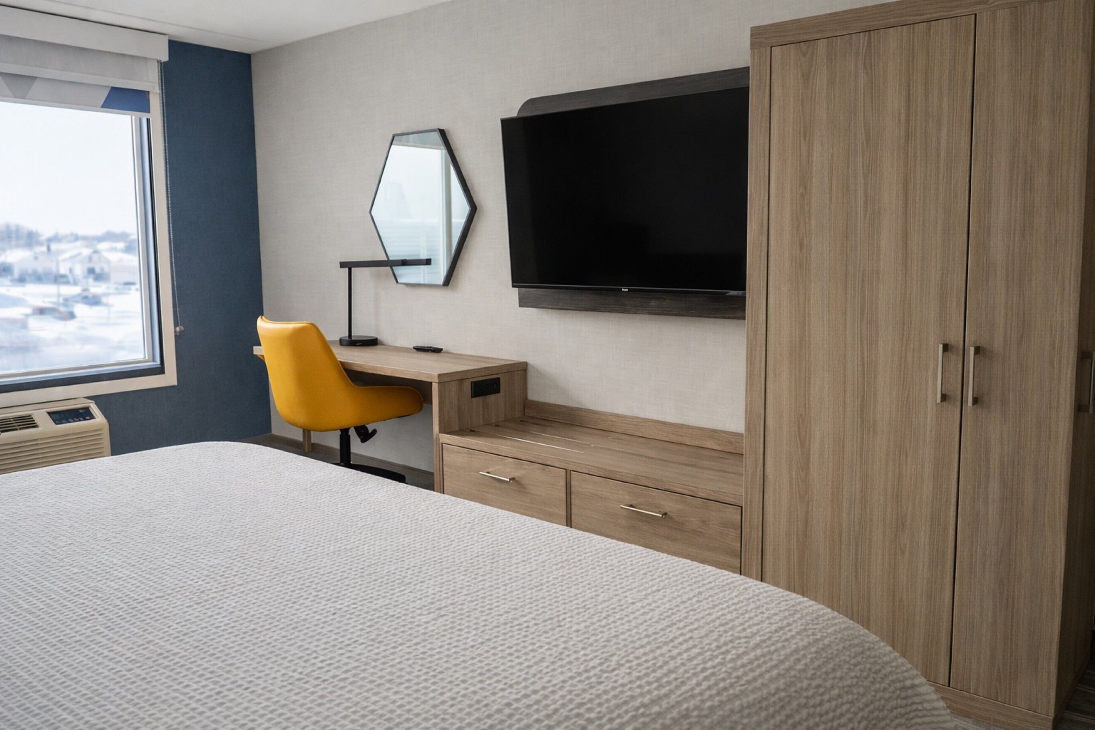 Una habitación de hotel con cama, escritorio, silla, televisor y armario.