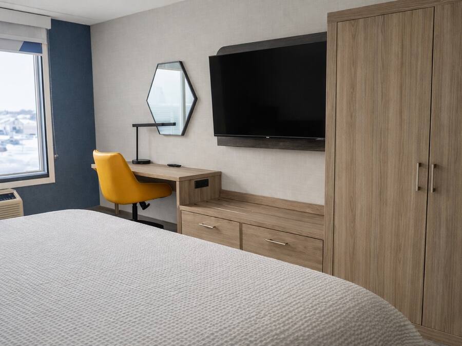 Una habitación de hotel con cama, escritorio, silla, televisor y armario.