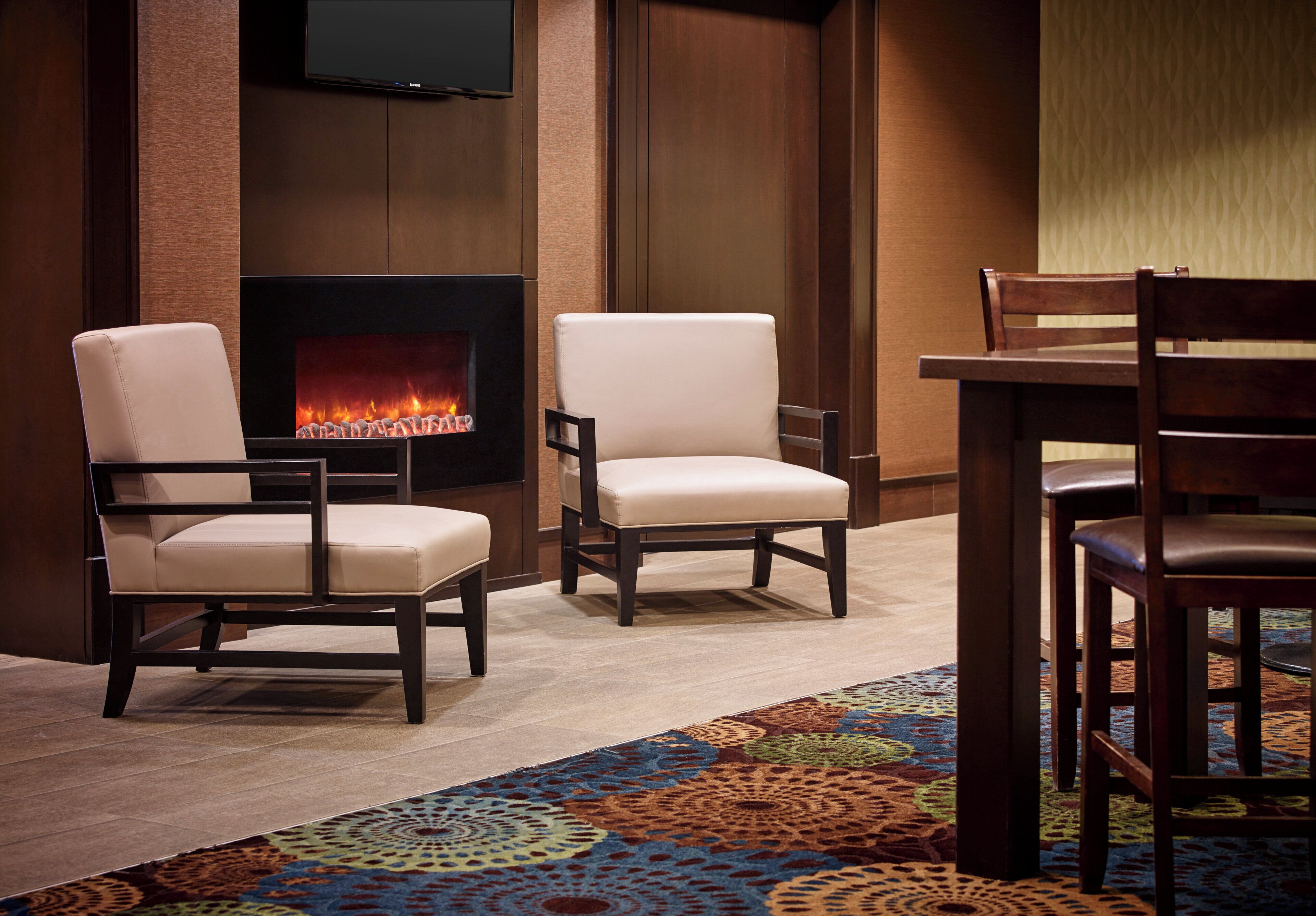 A room with a fireplace, two armchairs, a table, and a TV mounted on the wall.