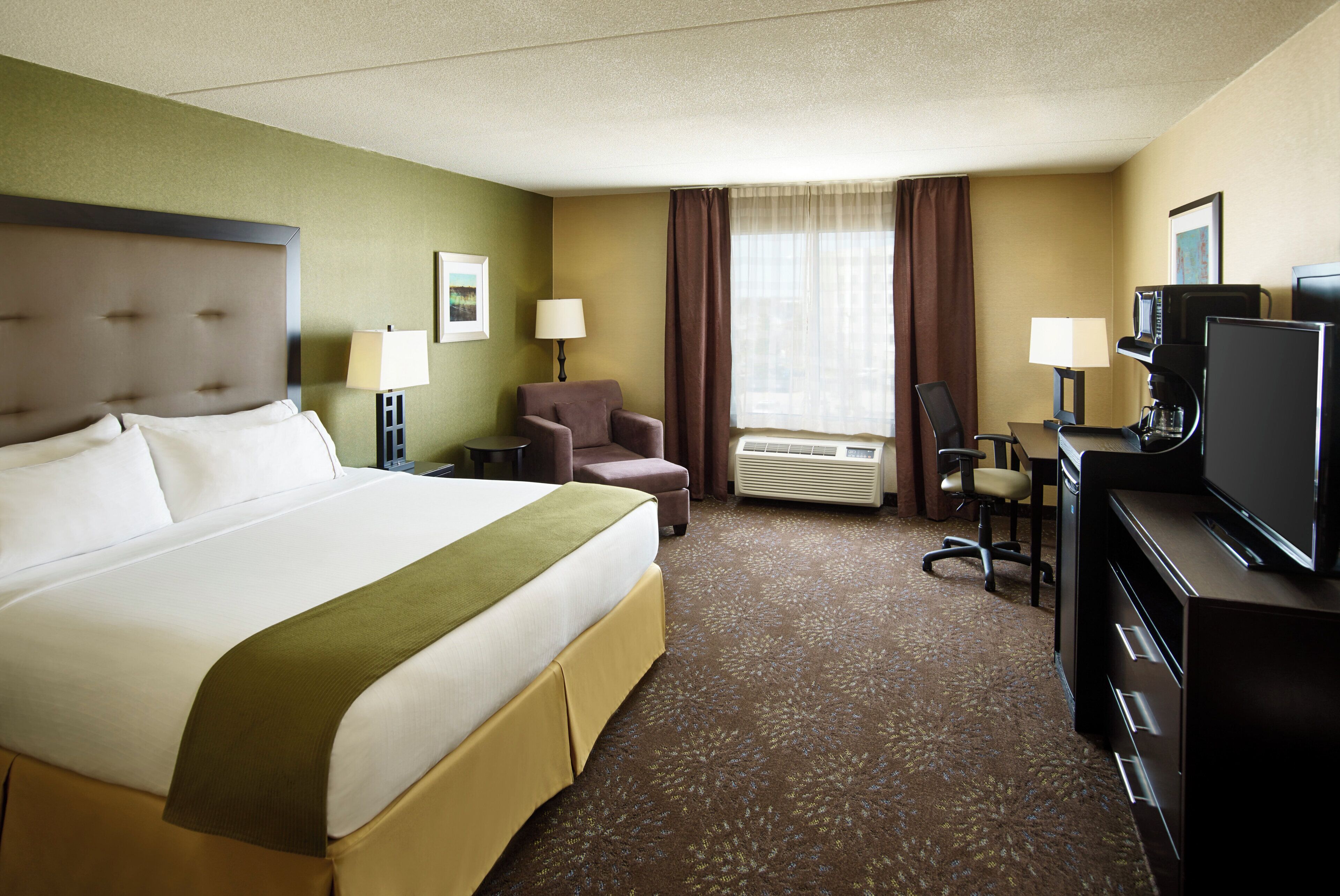 Une chambre d’hôtel avec un grand lit, un bureau avec un ordinateur, une chaise, une télévision et un appareil de climatisation.
