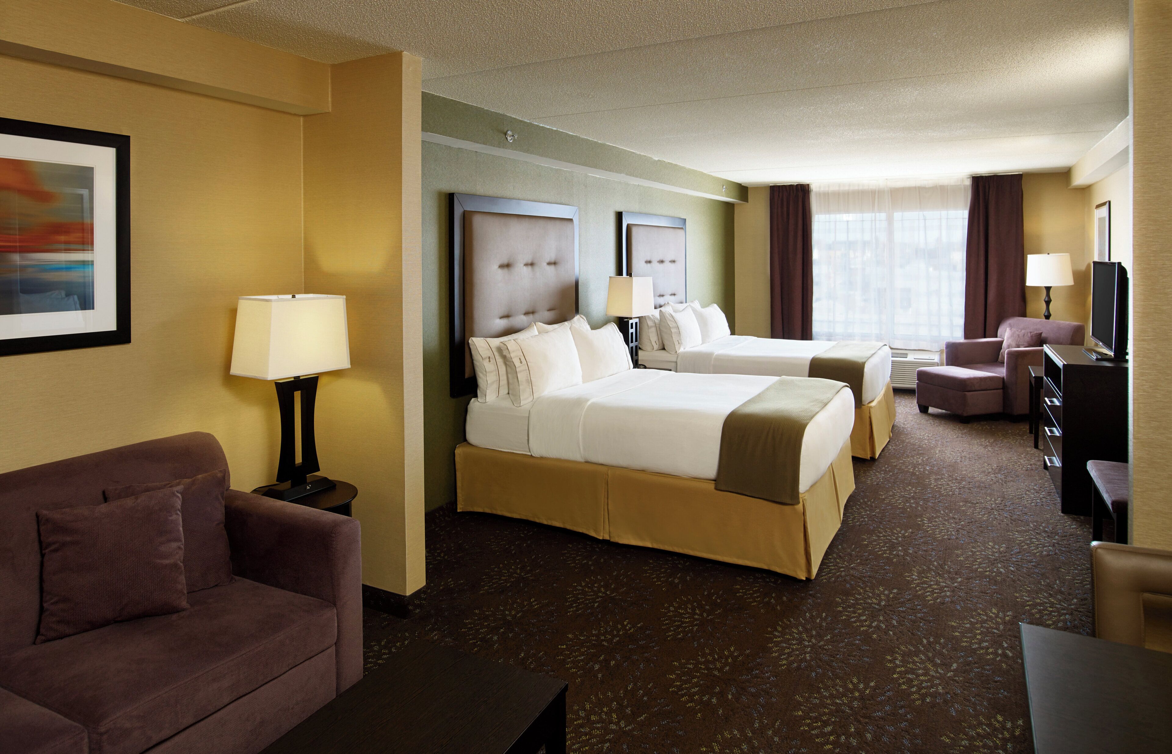 A hotel room with two beds, a sofa, a desk, and a television.