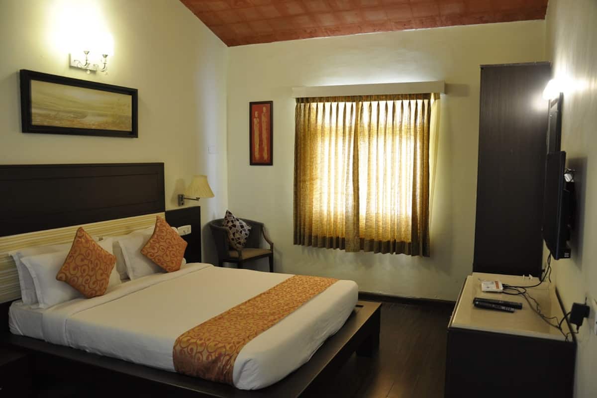 A hotel room with a large bed, a TV, a desk with a lamp, and a window with curtains.
