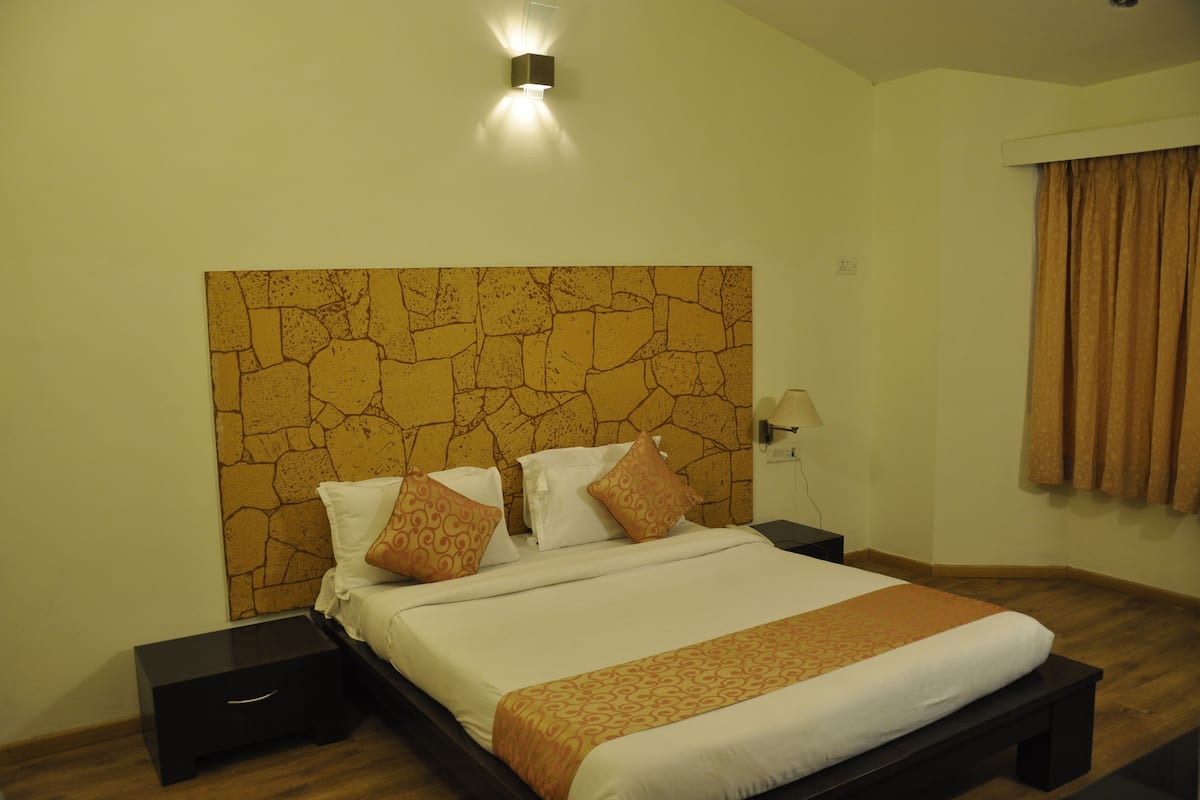 A neatly made bed with patterned pillows, a headboard with a stone-like texture, and a bedside lamp.